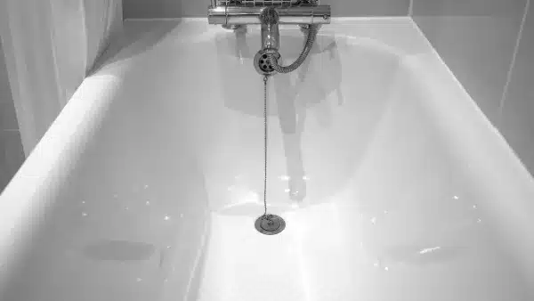 A close-up view of an empty white bathtub with a drain plug on a chain and a wall-mounted faucet above, ideal for demonstrating drain cleaning or maintenance.