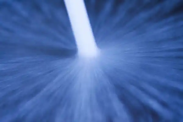 A close-up image of a white stream or jet of liquid spraying against a blue surface, creating a radial splash pattern.