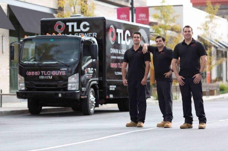 Three men in black uniforms stand in front of a black TLC Drain & Sewer service truck on a street, showcasing their expert Restoration Services as they confidently pose for the camera.